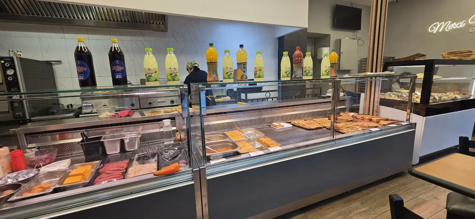 Le comptoir vitré : plats du jour alignés derrière la vitre, boissons au-dessus, salle en arrière-plan.