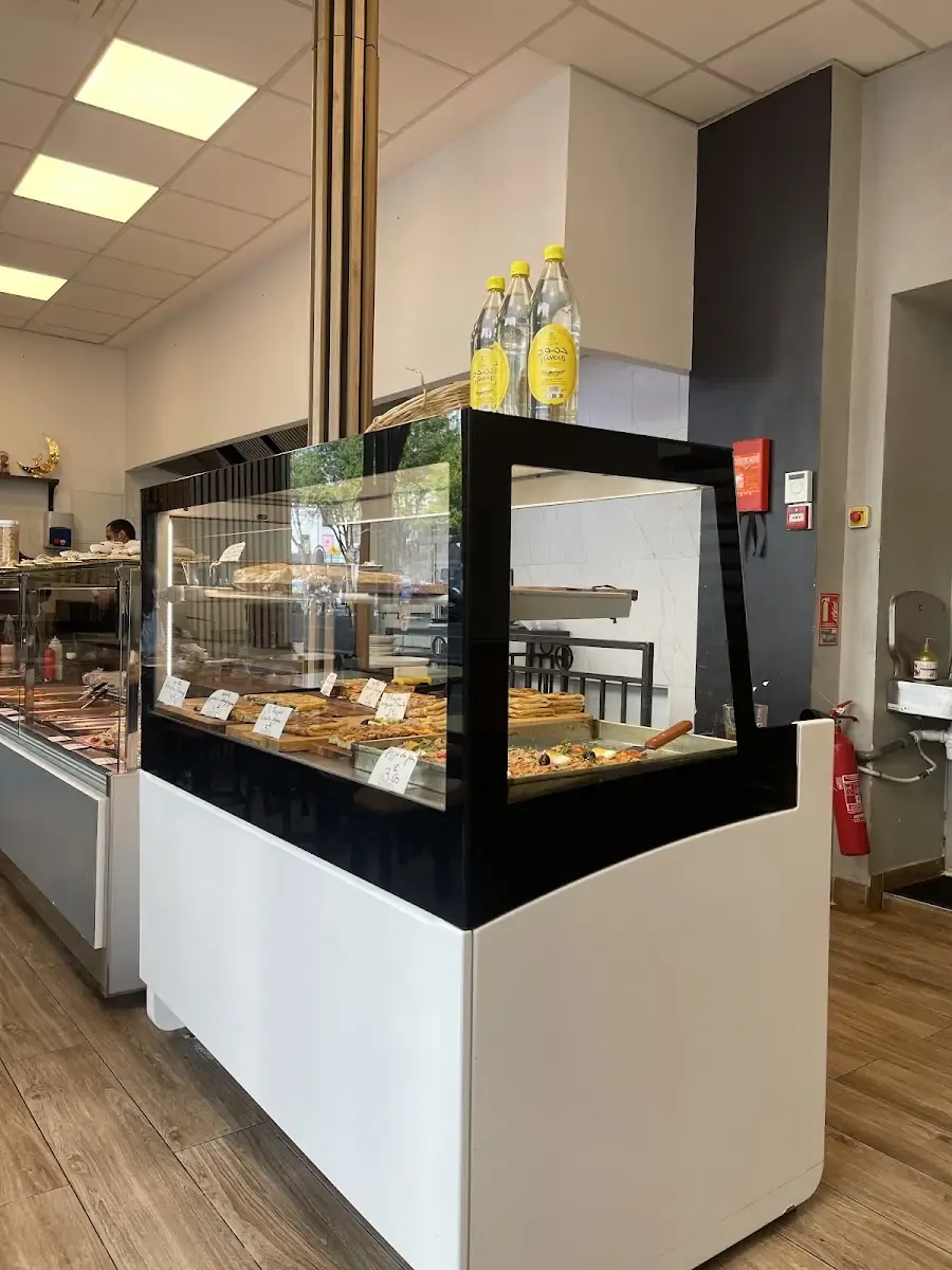 La salle : murs blancs, sol clair, vitrine réfrigérée et tables en bois.